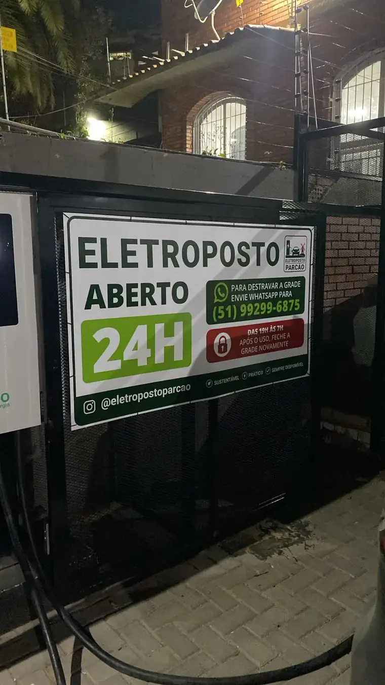 Placa do Eletroposto Parcão na rua: aberto 24h, com o WhatsApp para destravar a grade e o Instagram @eletropostoparcao
